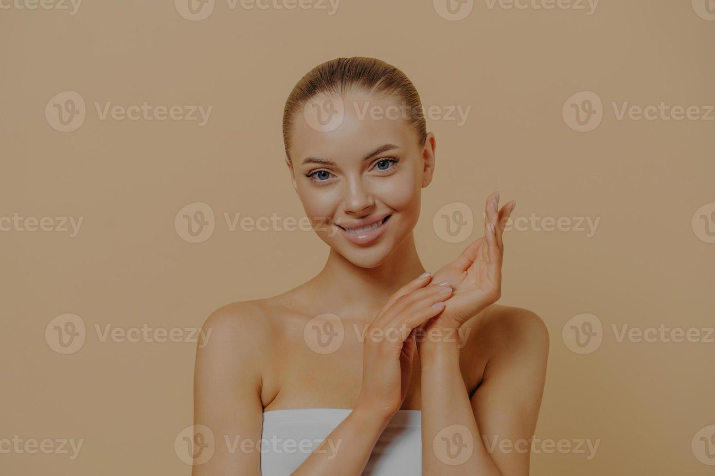 Young attractive woman using handcream to keep skin hydrated, touching hands after paraffin wax bath photo