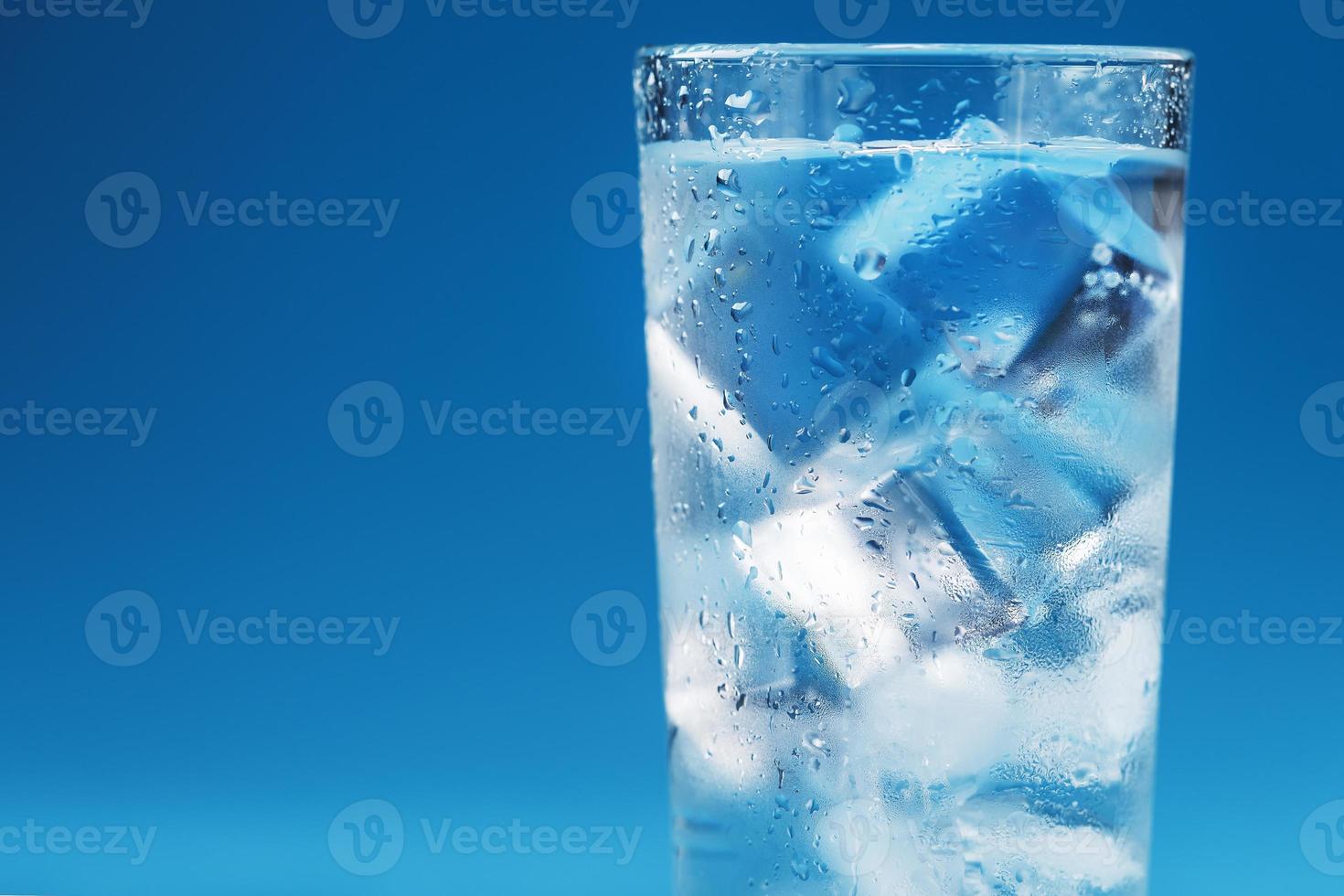 un vaso con agua helada y cubitos de hielo sobre un fondo azul. foto