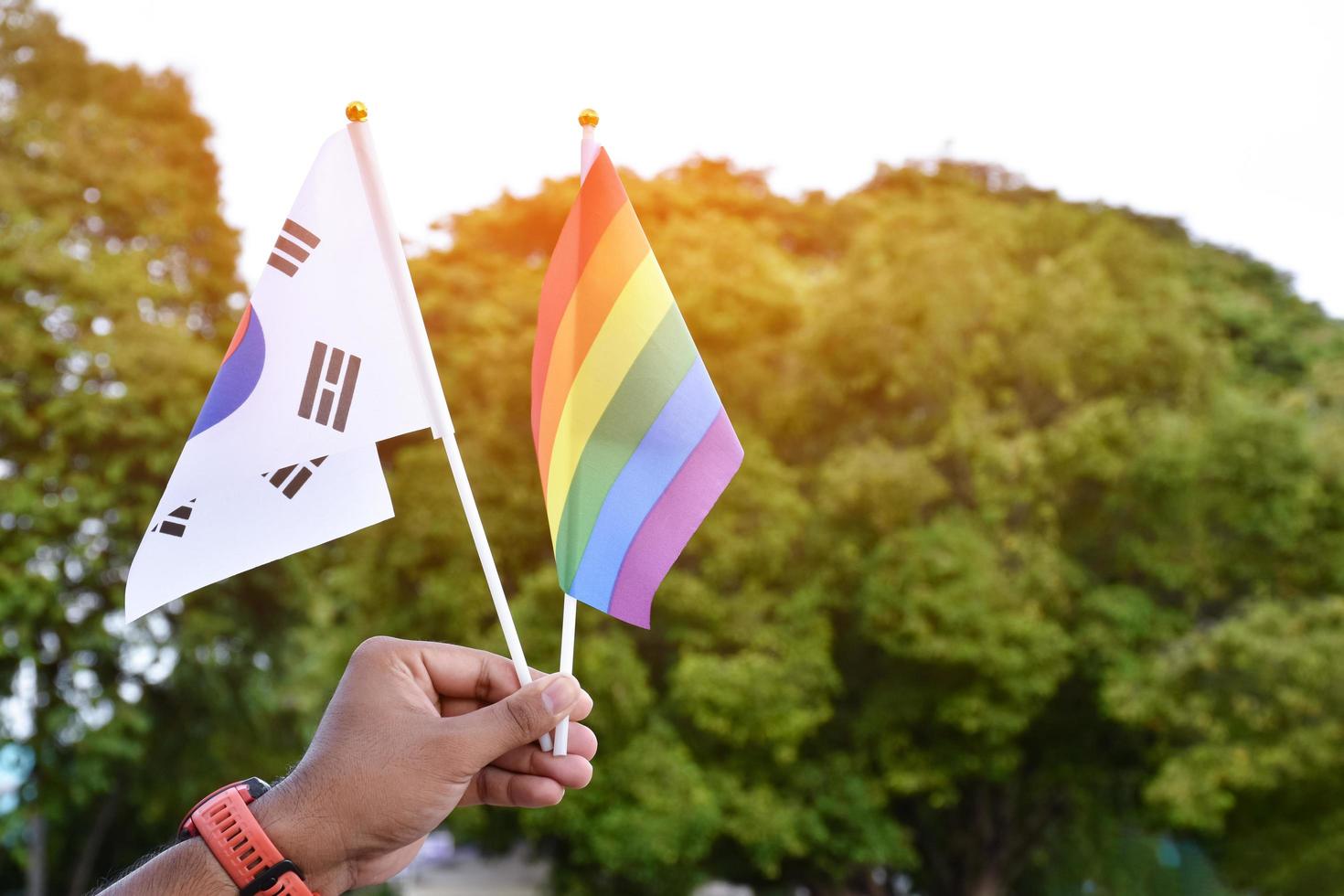 bandera del arco iris y bandera nacional de corea del sur sosteniendo en la mano, enfoque suave y selectivo, concepto para la celebración de lgbtq plus en el mes del orgullo en todo el mundo. foto