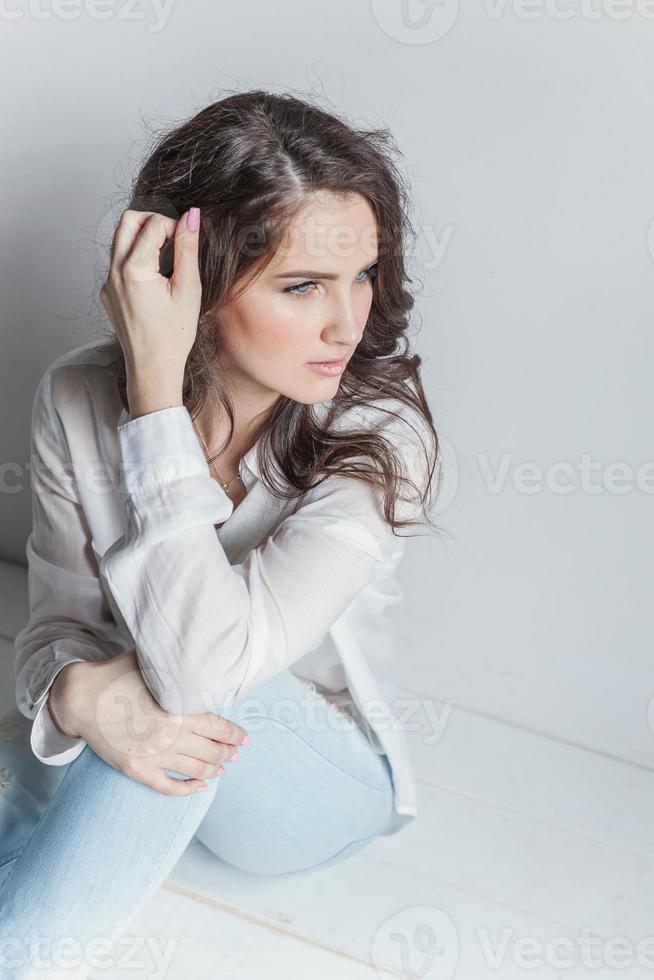 Girl in bright room sitting against white wall photo