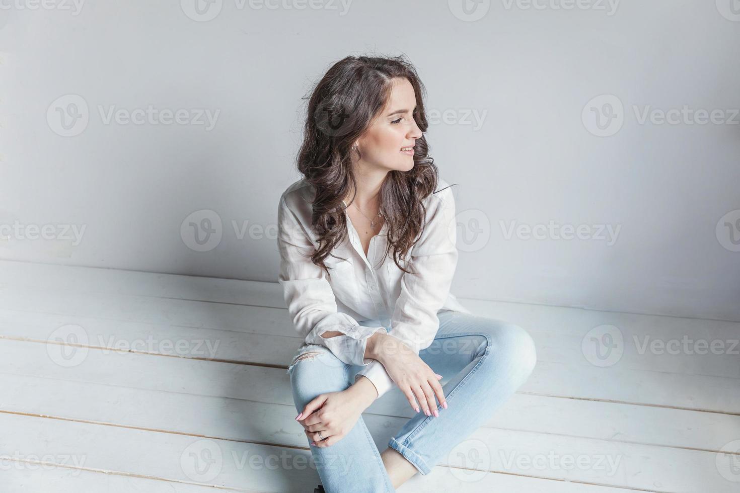 Girl in bright room sitting against white wall photo