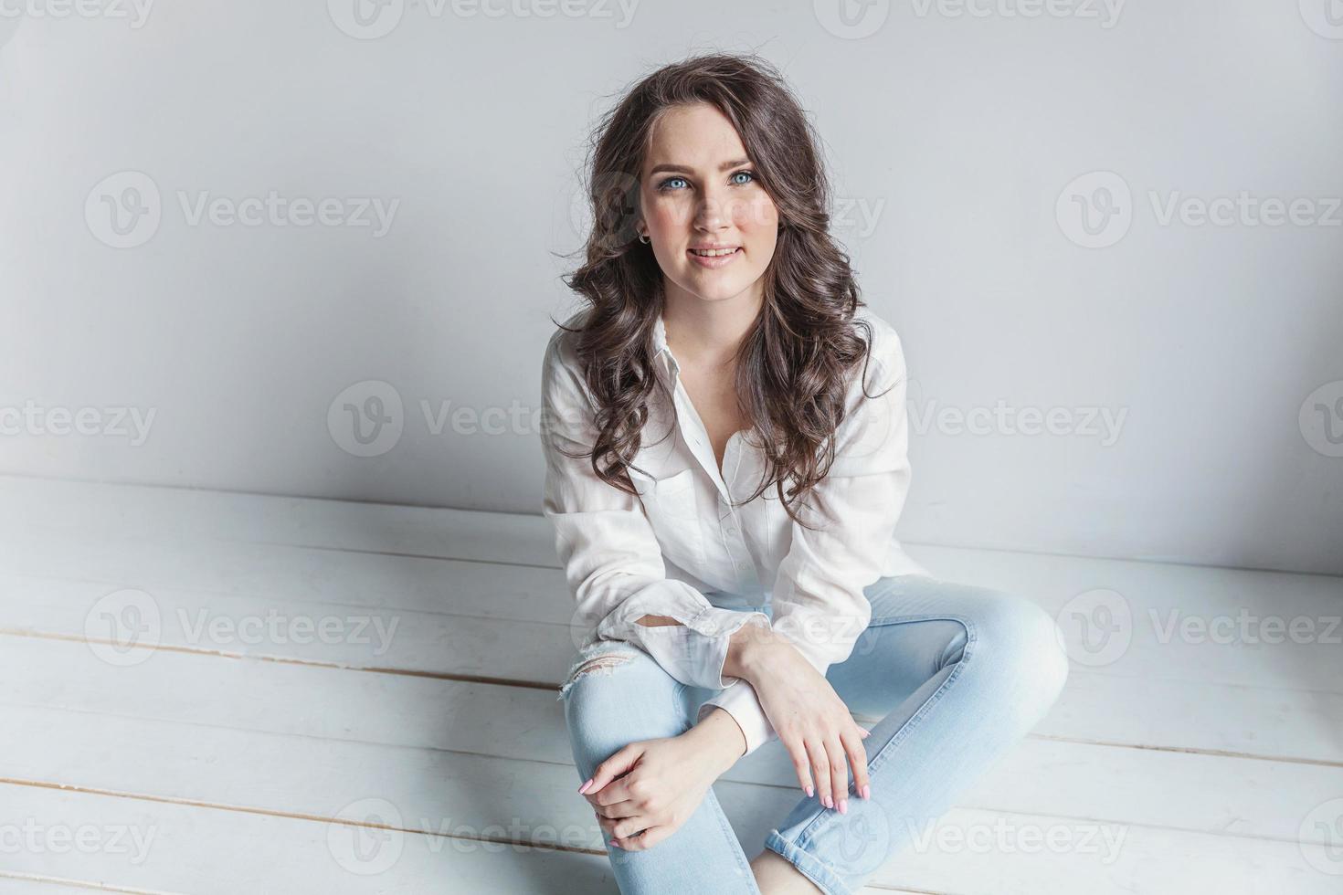 Girl in bright room sitting against white wall photo