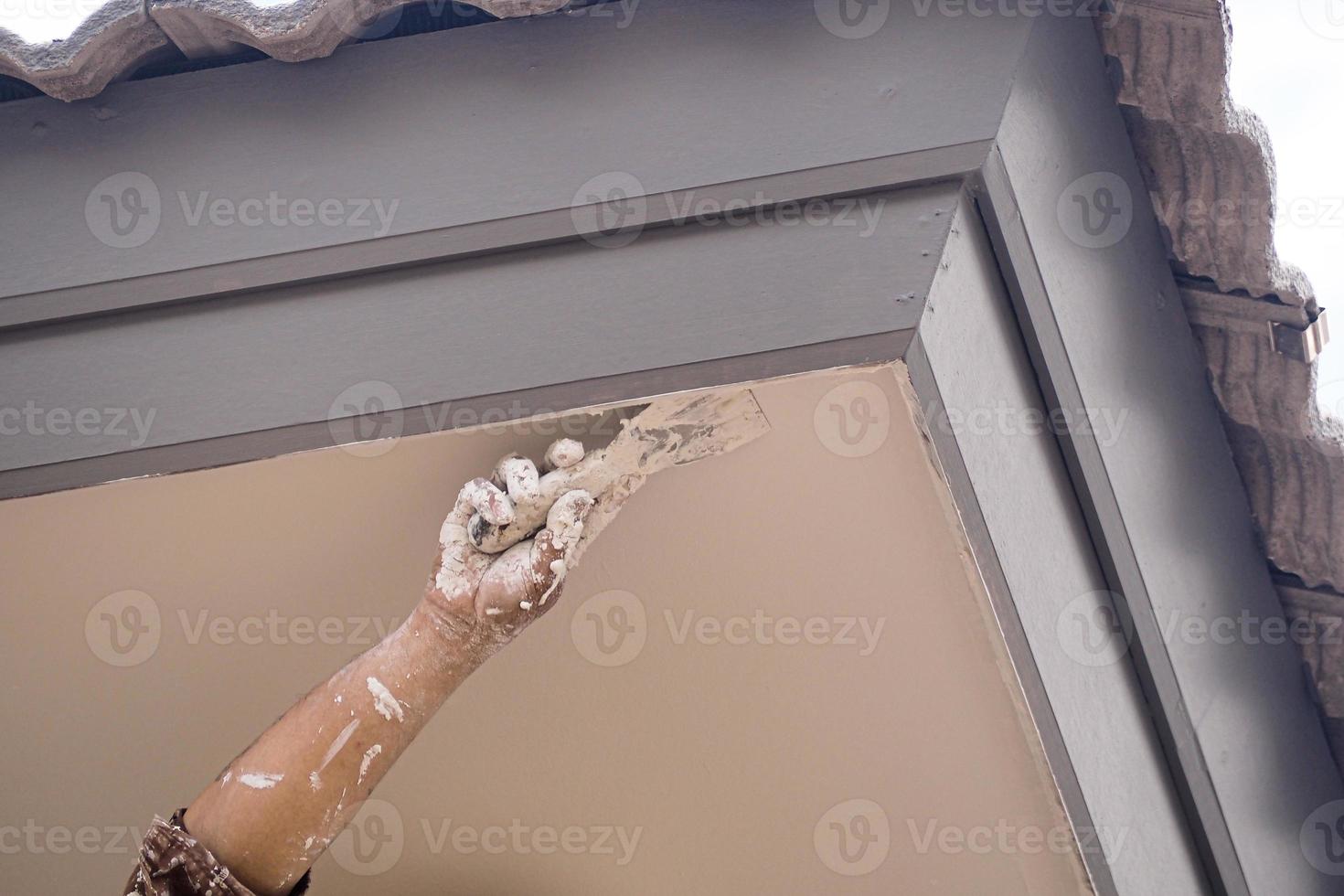 A painter is painting the exterior under the eaves of a gray concrete roof. photo