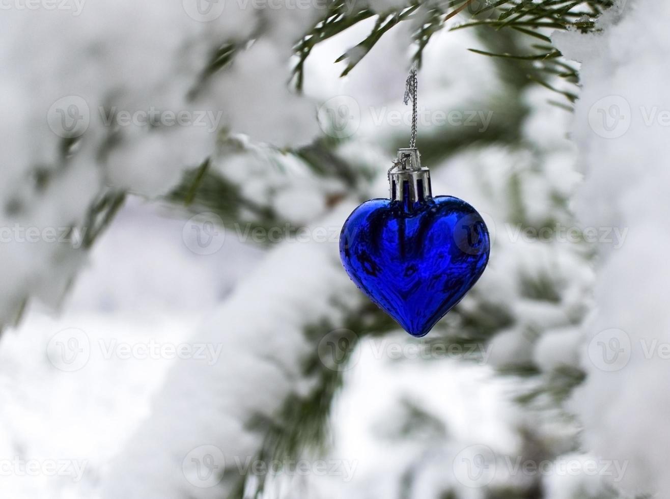 fondo de navidad con árbol de navidad juguete corazón azul en la rama de pino cubierto de nieve en el bosque de invierno con espacio de copia vacaciones de año nuevo, celebración de navidad, tarjeta de felicitación foto