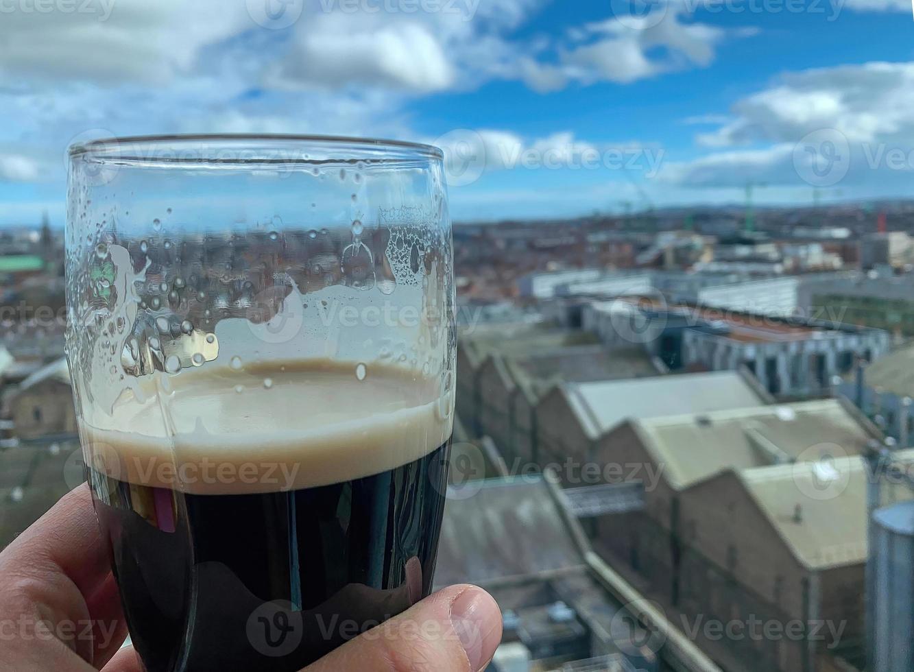 mano sosteniendo una cerveza con vista a la azotea foto