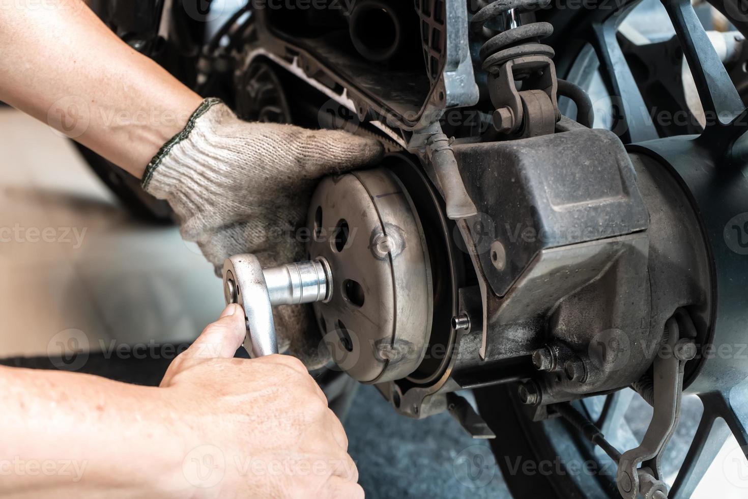 Mechanic using wrench and socket to Remove auto Transmission system or Rear Clutch Pulley of scooter Motorcycles,working in garage maintenance, repair motorcycle concept .selective focus photo