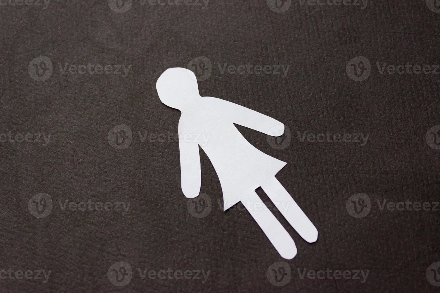 Silhouette of a woman in dress of white paper, cut by hand. In the center of photo on black background