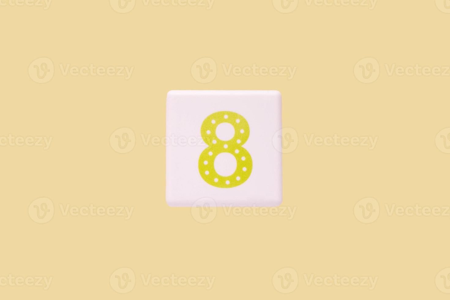 Close-up photo of a white plastic cube with a yellow number 8 on a yellow background. Object in the center of the photo