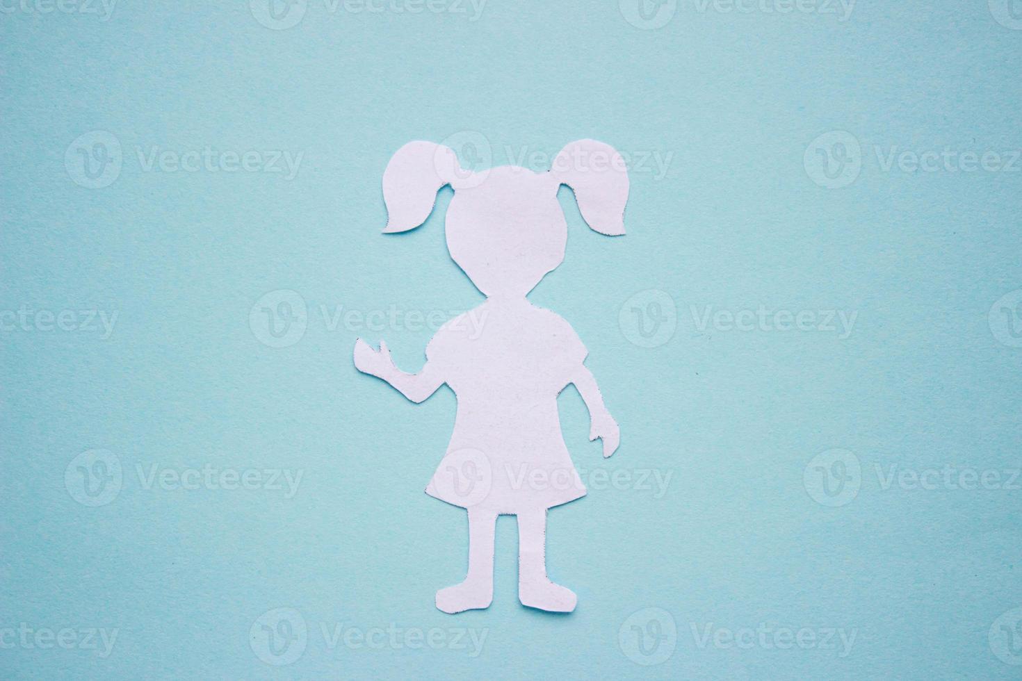 The form of a girl in a dress and with ponytails made of white paper, cut by hand. In the center of the photo