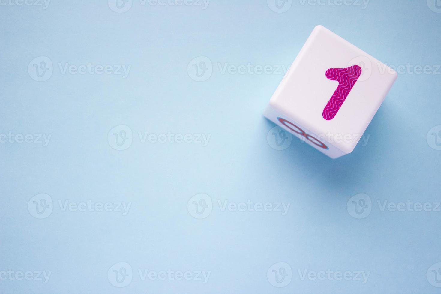 Close-up photo of a white plastic cube with a purple number 1 on a blue background in the upper right corner. With copy space