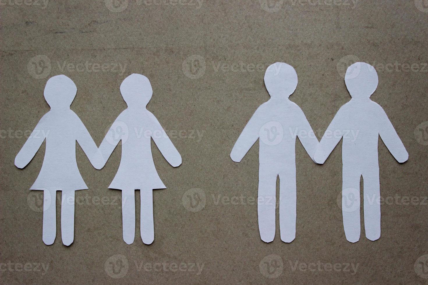 Two same-sex couples of people holding hands cutting from white paper on beige. A couple of women and a couple of men. Concept of same sex love, relationship, gender identity photo