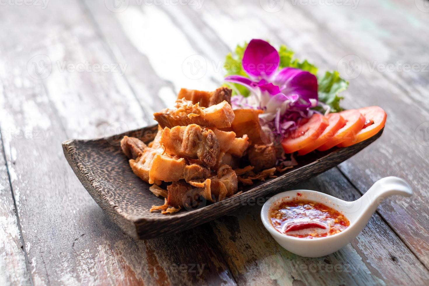 panceta de cerdo frita con sal en un plato natural con cáscara de coco y salsa picante en una mesa de madera foto