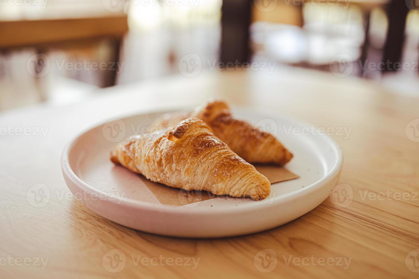 Two appetizing croissants on a plate are placed on a wooden table in the cafe. photo