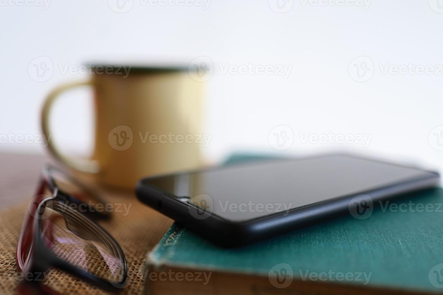 Yellow coffee mugs, phones and books on the wooden table inside the house. photo