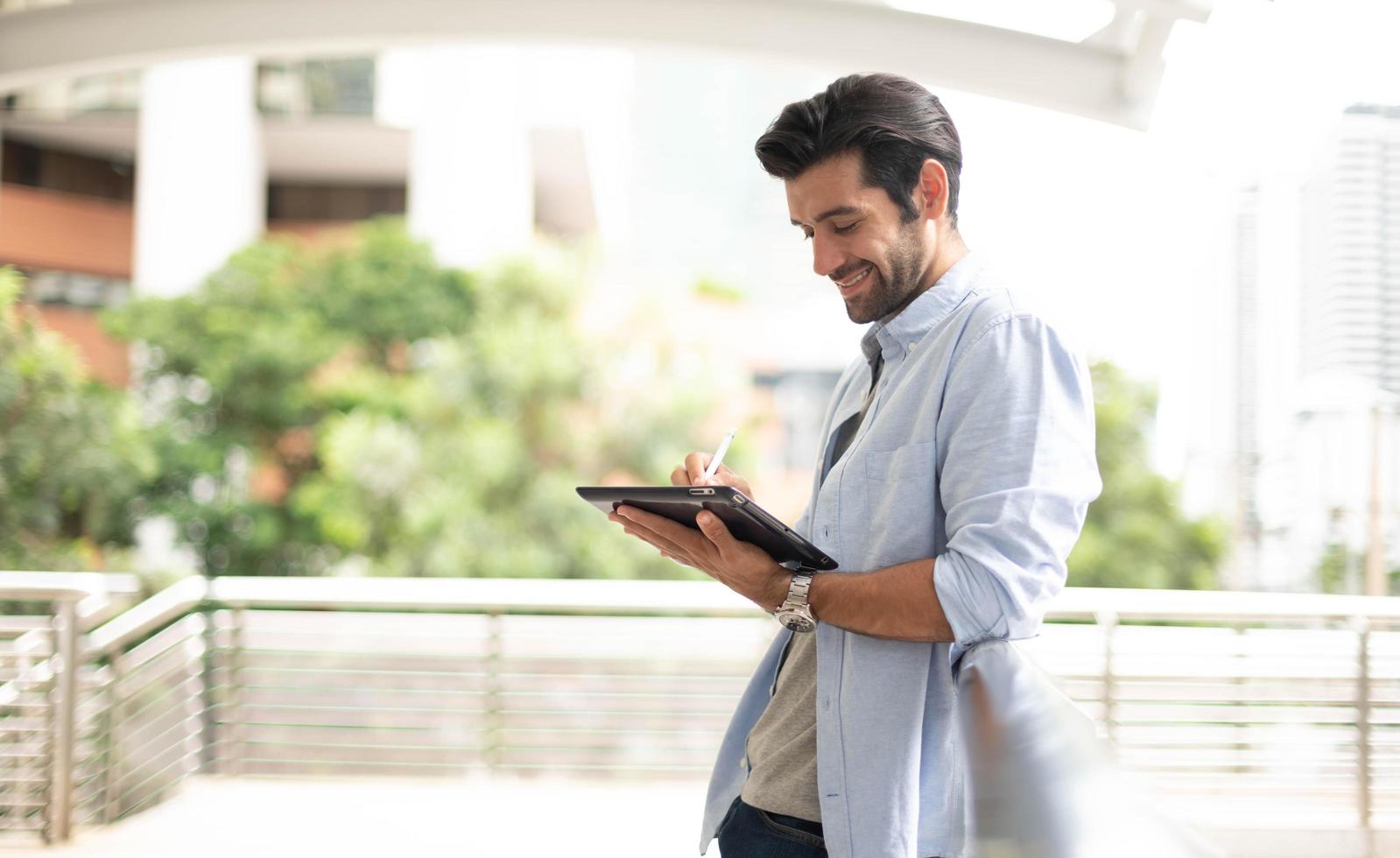 el joven que usa una tableta para fuera de la oficina. el hombre vestido con casual y sintiéndose relajado y feliz. 13091919 Foto de stock en Vecteezy