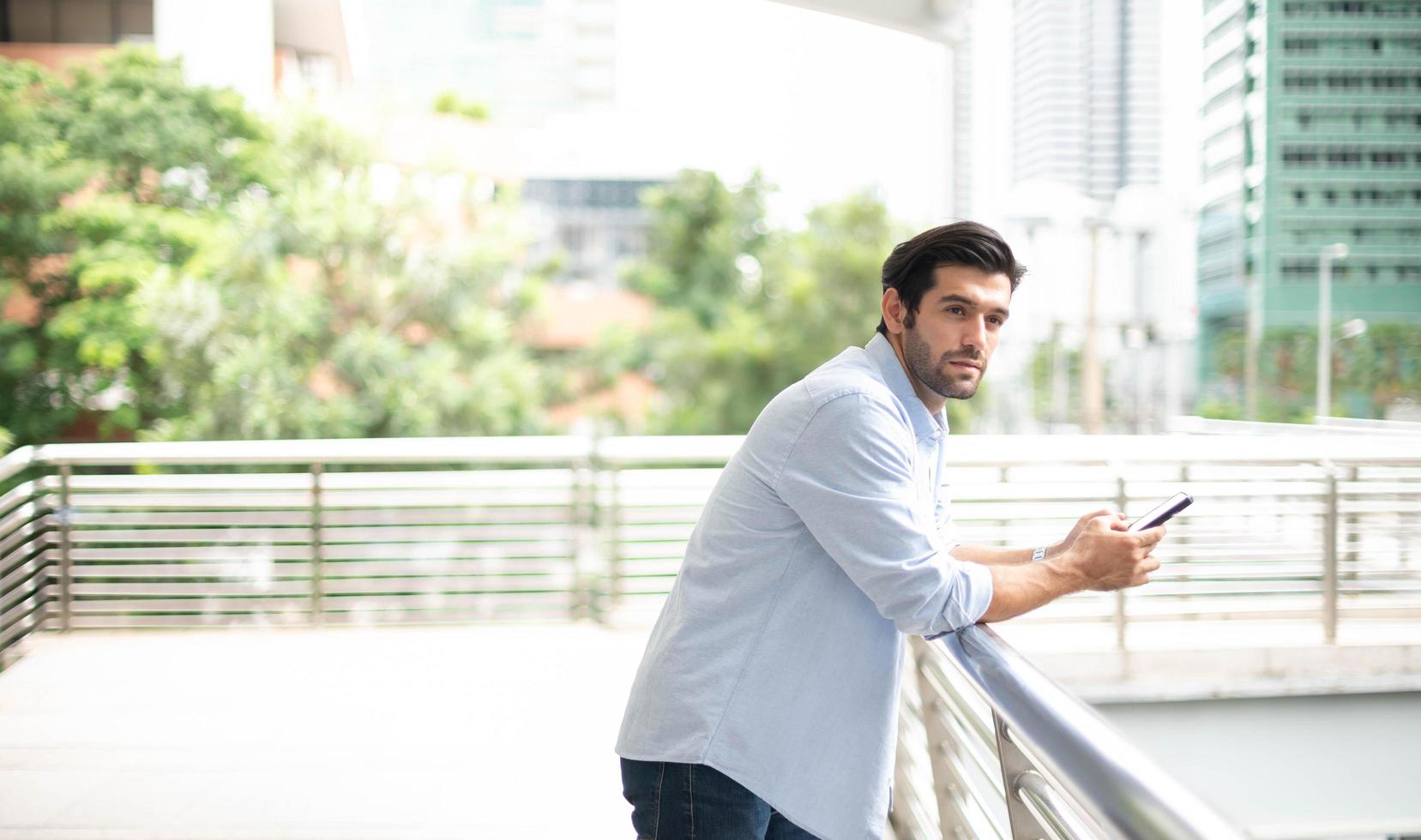 Young caucasian man using smart phone and smiling while waiting his friend at the outside. photo