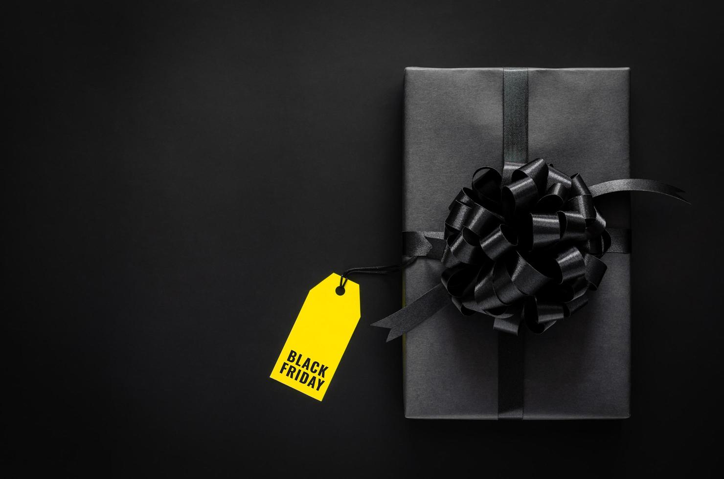 A black gift box with ribbon and yellow price tag puts on black background. Black friday concept. photo