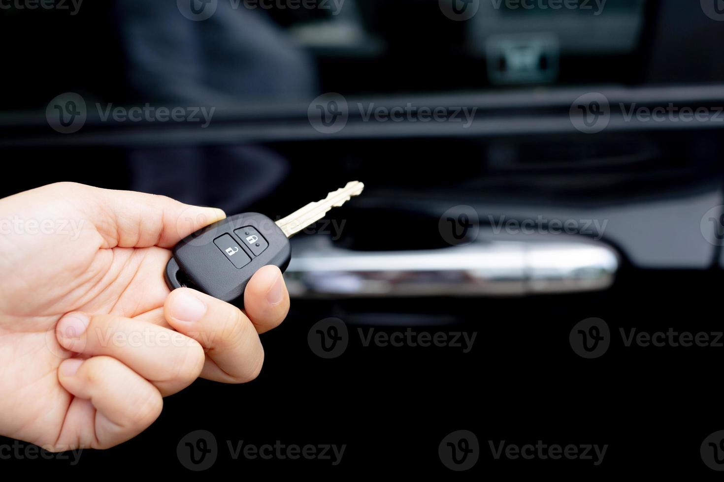 A man holding a car key in front of a car at a showroom photo