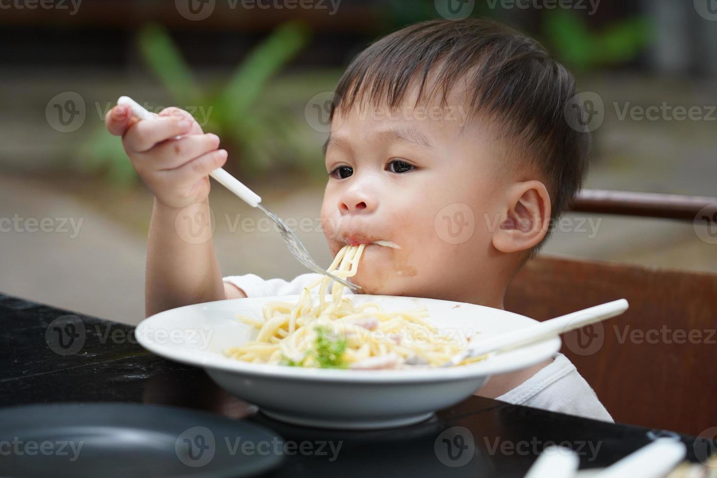 little boy eating spaghetti with deliciousness, learning concept for toddlers photo