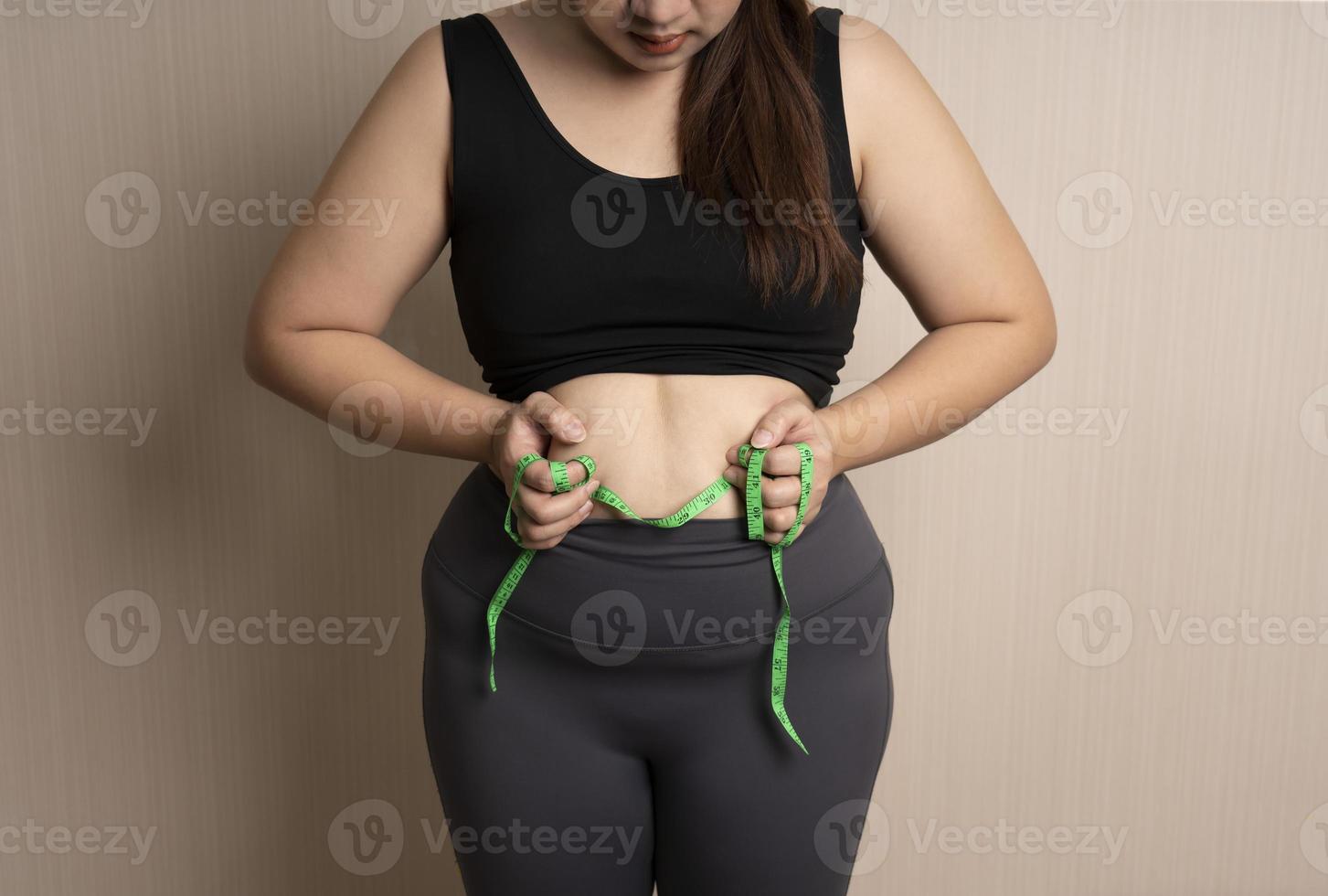 beautiful fat woman in sportswear catches her big belly or belly fat with tape measure. healthy weight control concept. overweight, bloated belly photo