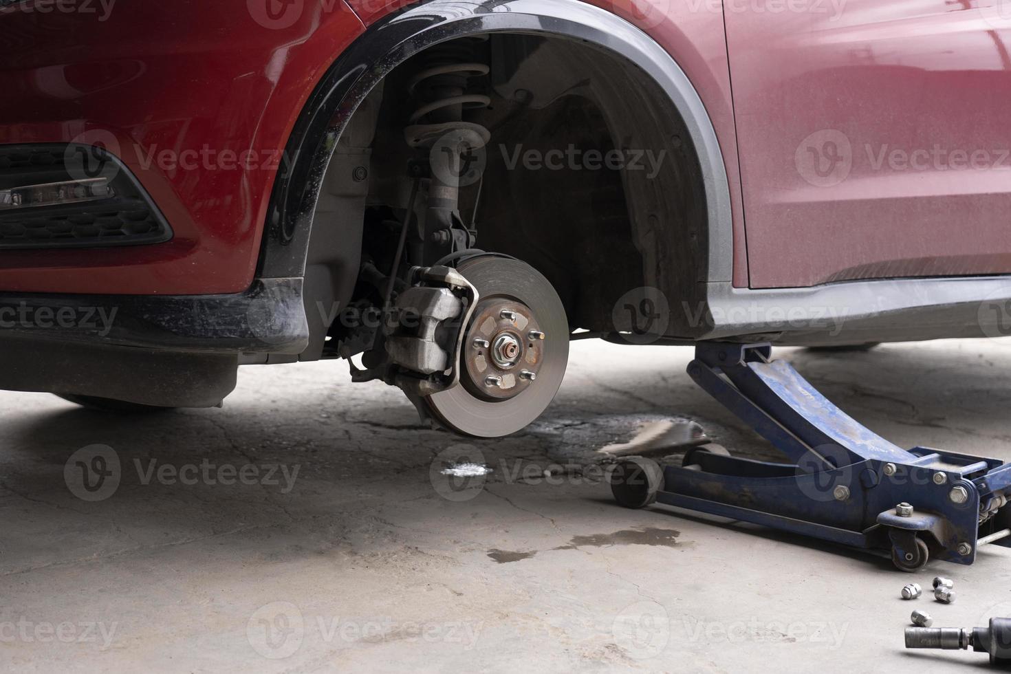 sustitución de la rueda del coche con gato hidráulico. concepto de mantenimiento de automóviles. Retire las ruedas del automóvil en preparación para el parche de neumáticos. discos de freno sin ruedas. centro de servicio de reparación de automóviles foto