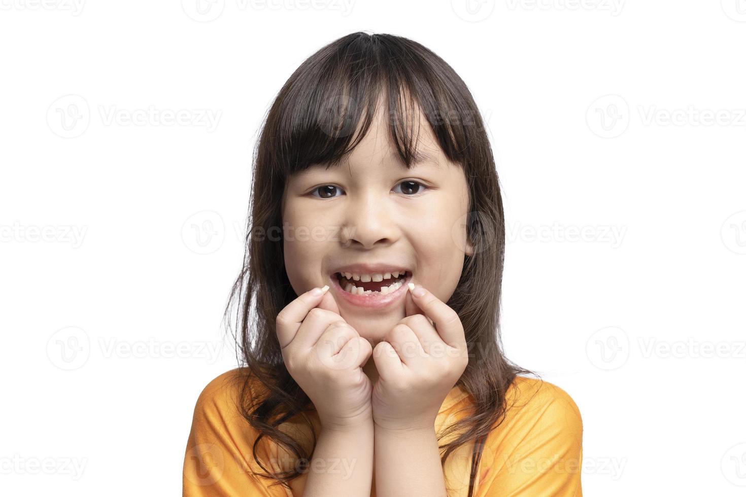 Cute Asian girl smiles showing her missing teeth in her mouth and holding her loose teeth. Tooth loss by age concept, replacement of permanent teeth. Tooth removal. photo