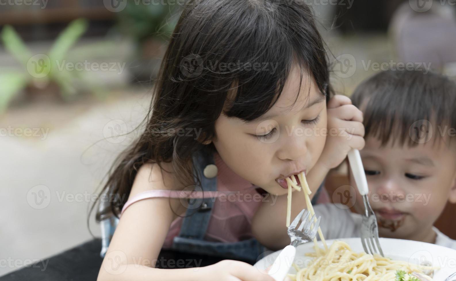 los niños y niñas asiáticos están comiendo espaguetis con delicias. hermana y hermano están comiendo espagueti foto