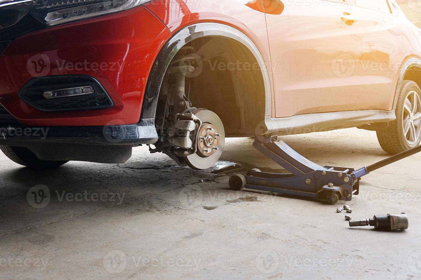 sustitución de la rueda del coche con gato hidráulico. concepto de mantenimiento de automóviles. Retire las ruedas del automóvil en preparación para el parche de neumáticos. discos de freno sin ruedas. centro de servicio de reparación de automóviles foto