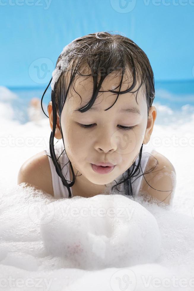 Close up of a cute girl blowing white soap bubbles in her hand in a swimming pool at home. happy family holiday concept. child's happy face, child happiness, water and soap bubbles, vertical photo
