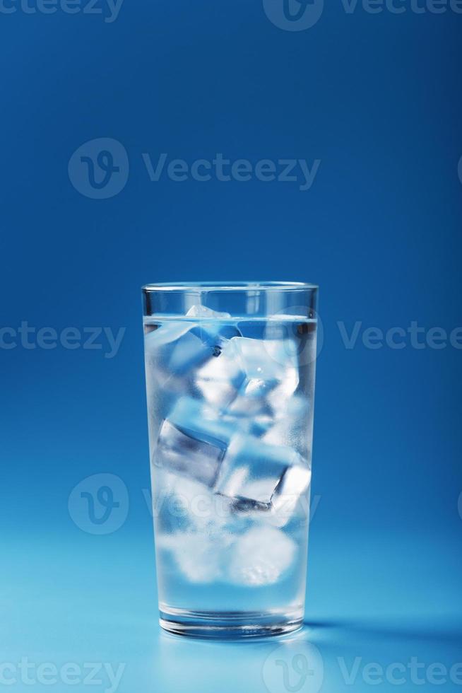 un vaso con agua helada y cubitos de hielo sobre un fondo azul. foto