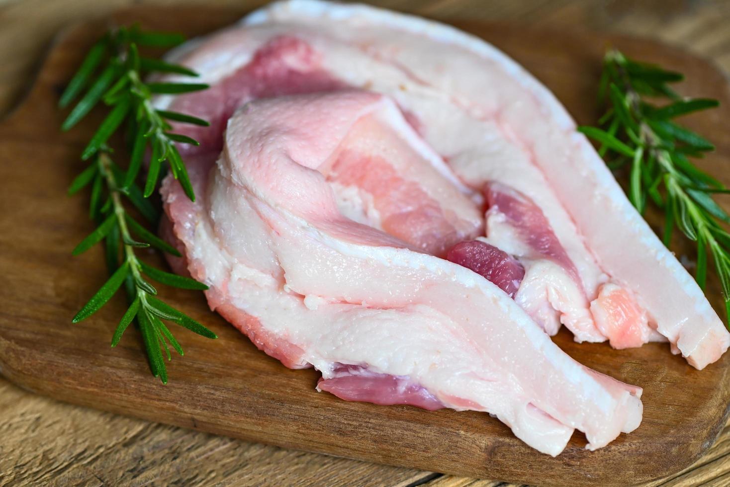 cerdo en un plato de madera con romero, carne de cerdo fresca y cruda para cocinar, piel de cerdo - vista superior foto