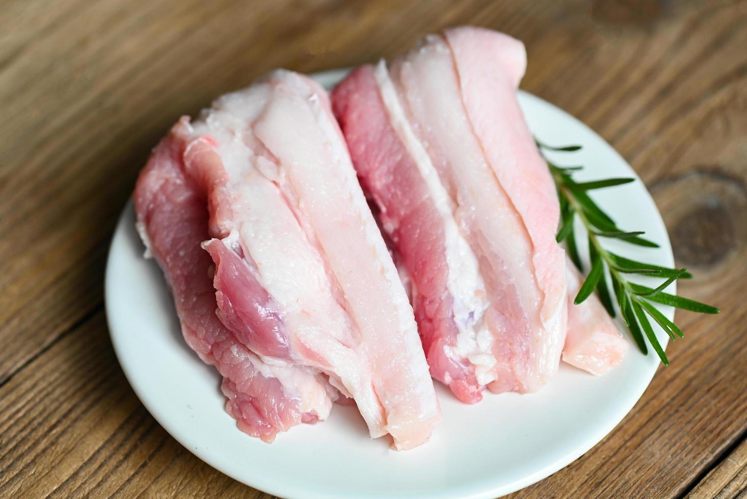 pork on wooden plate with rosemary, fresh raw streaky pork meat for cooking food, pork skin pig skin - top view photo