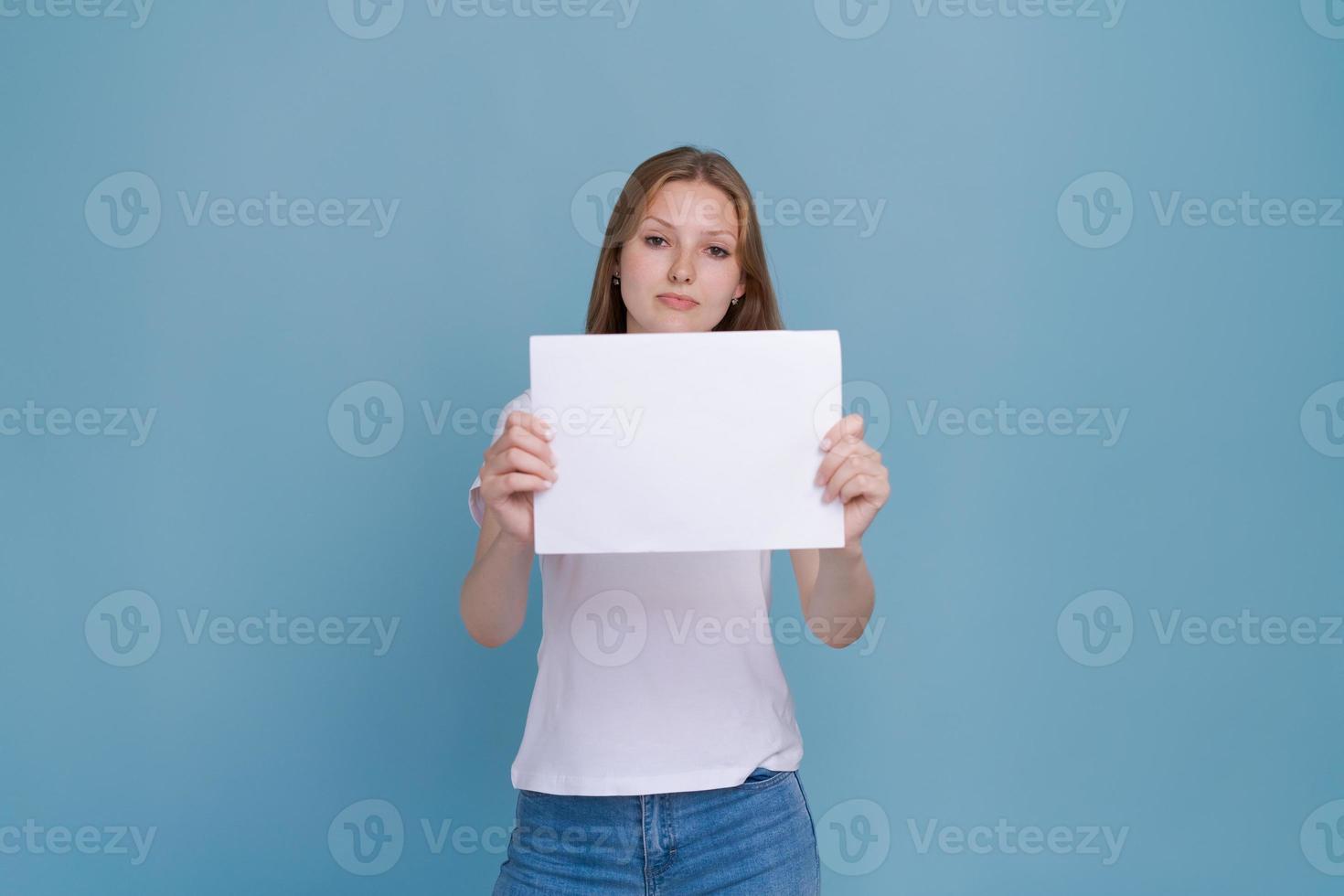 Young woman holding white paper on blue background. Caucasian woman with white photo