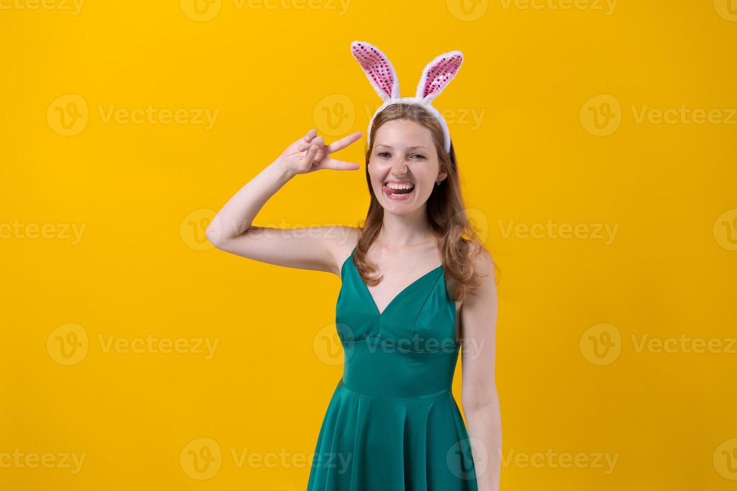 Shot happy girl in fluffy pink bunny ears, points fingers to side, demonstrates photo