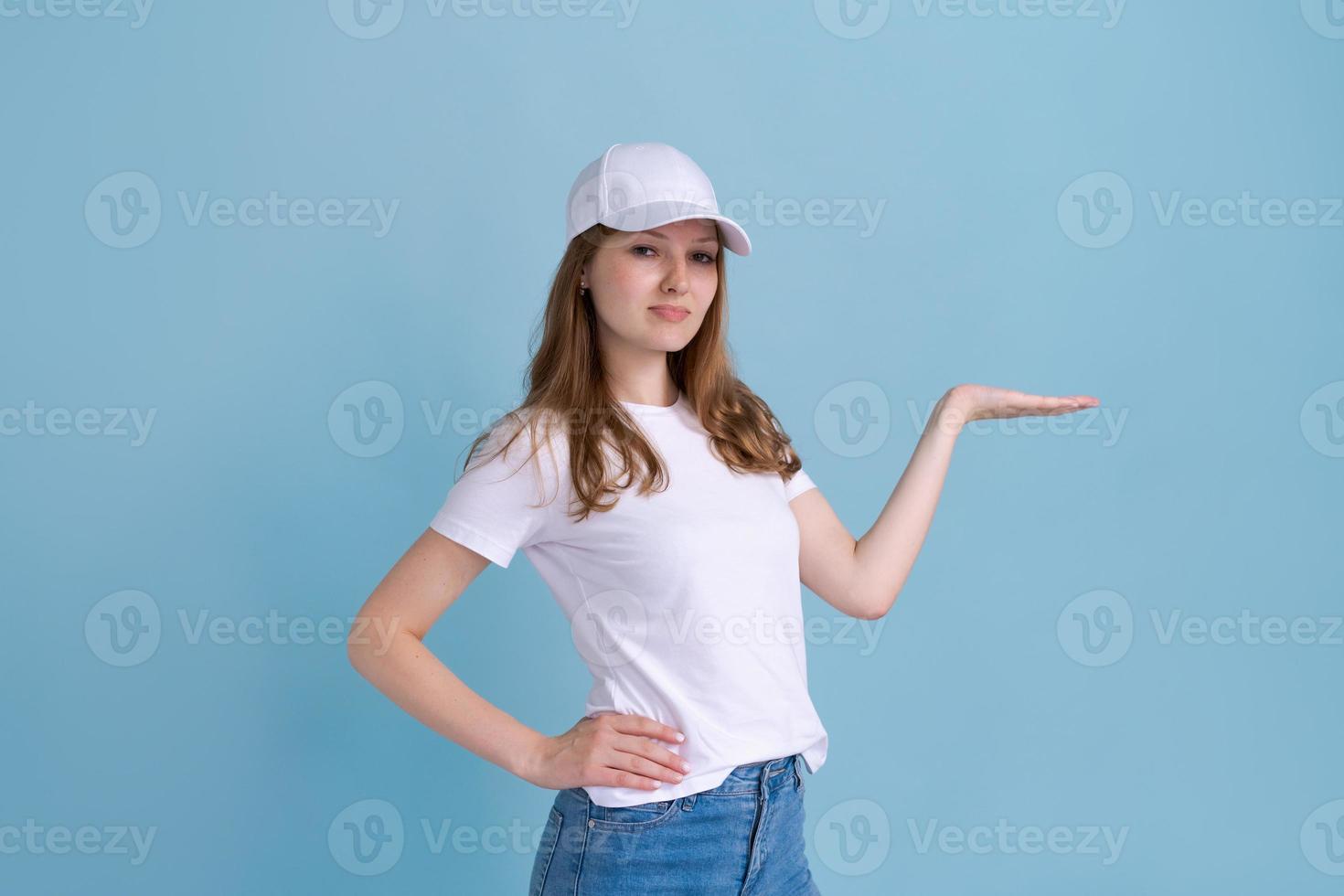 Caucasian woman in white t-shirt and cap on blue background, pointing to side photo