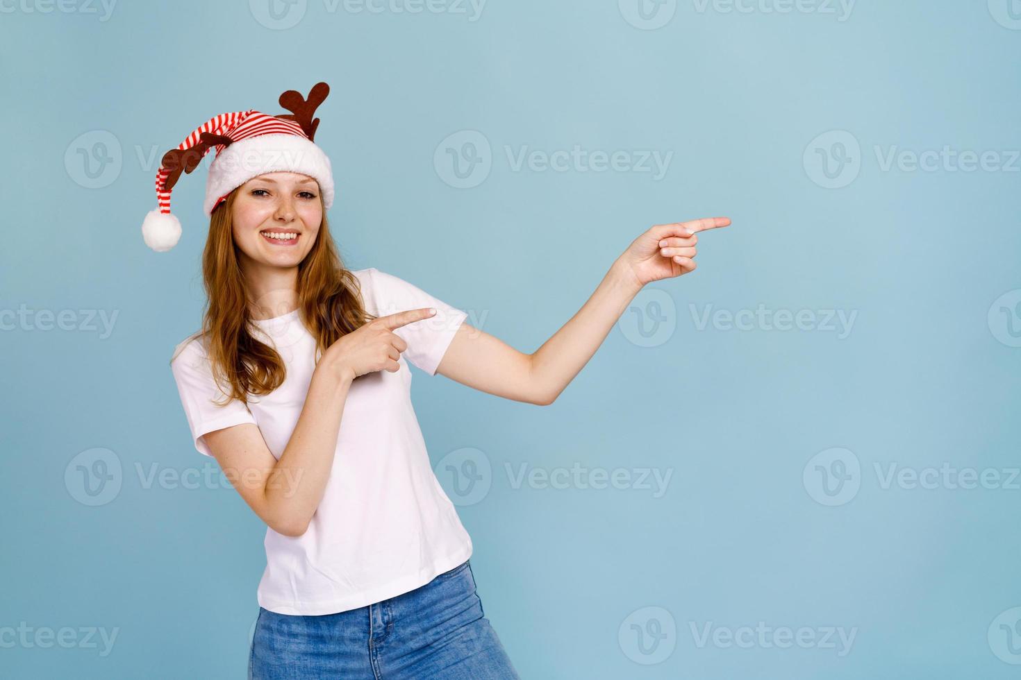 Cheerful santa girl in funny decorative deer antlers, pointing with forefinger photo