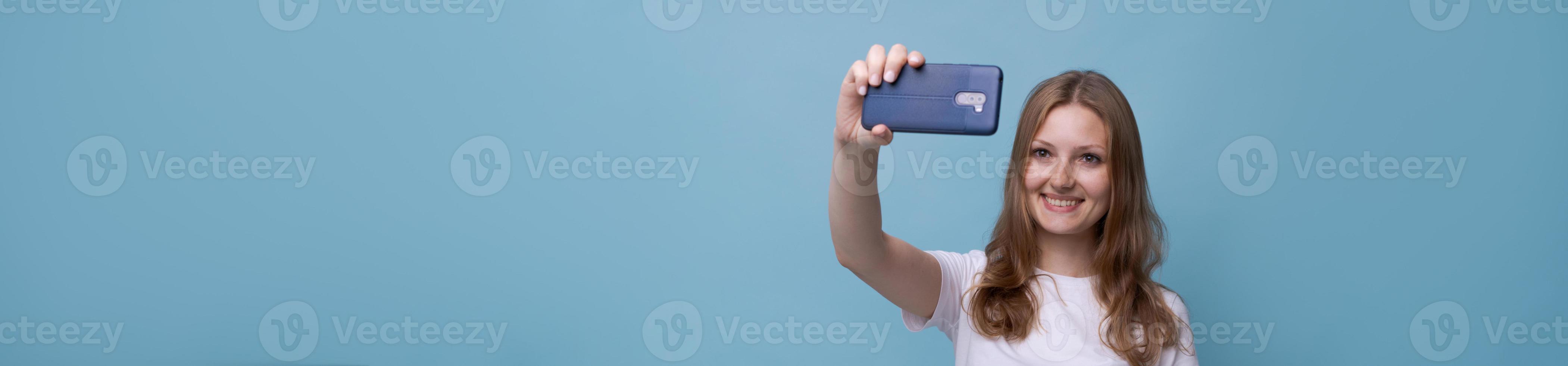 A young woman vlogger with a surprised face takes a picture of herself on the photo