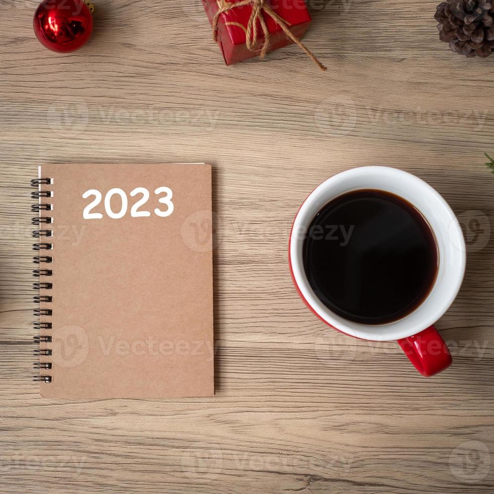 2023 notebook, black coffee cup and Christmas gift on wood table, Top view and copy space. Xmas, Happy New Year, Goals, Resolution, To do list, Strategy and Plan concept photo