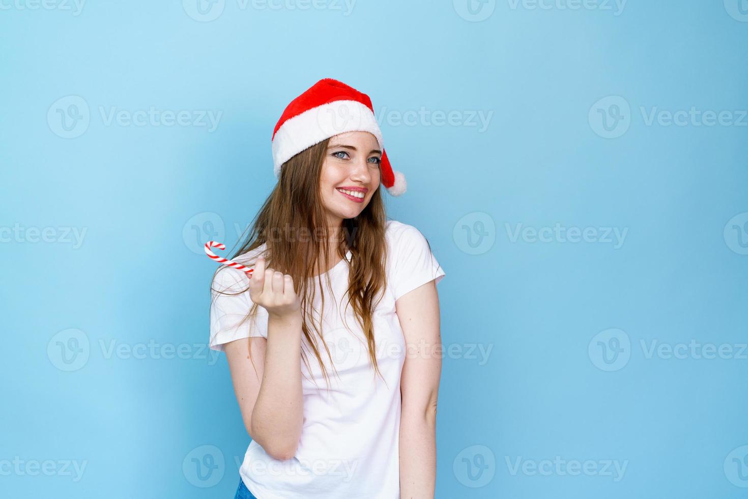 Pretty woman in santa hat holding red and white christmas lollipop in white photo