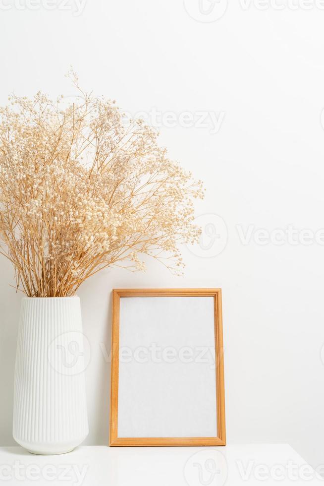 Wooden vertical frame with white vase of gypsophila flowers over white wall photo