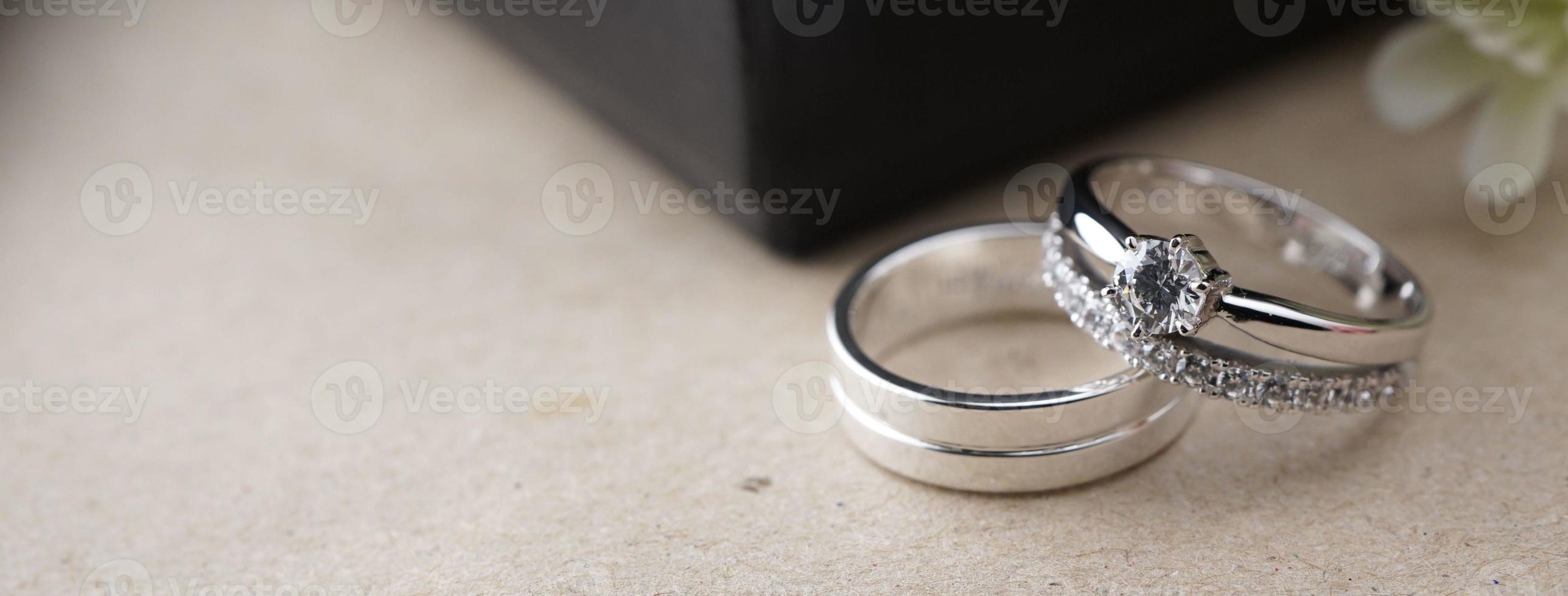 White gold wedding ring with a bird laser on the ring surface. With a black ring box background and artificial flowers. On the left there is an empty space to fill in text photo