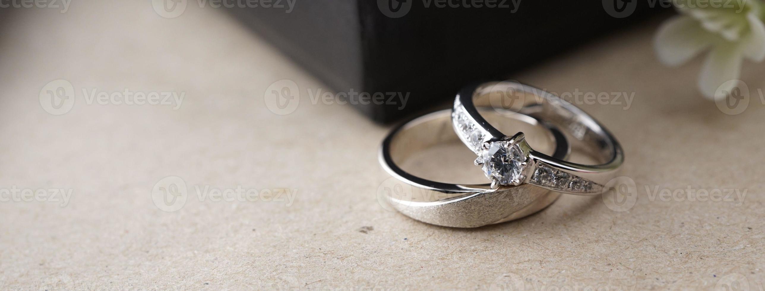 White gold wedding ring with a bird laser on the ring surface. With a black ring box background and artificial flowers. On the left there is an empty space to fill in text photo
