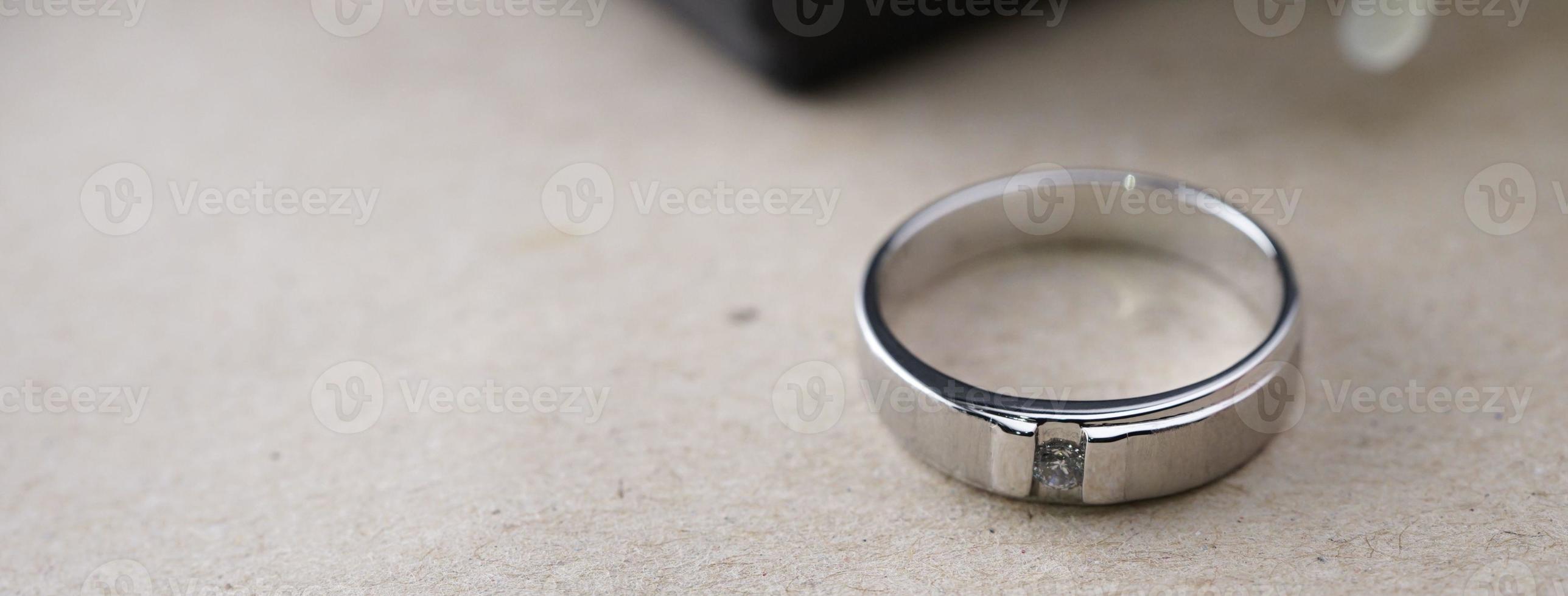 White gold wedding ring with a bird laser on the ring surface. With a black ring box background and artificial flowers. On the left there is an empty space to fill in text photo