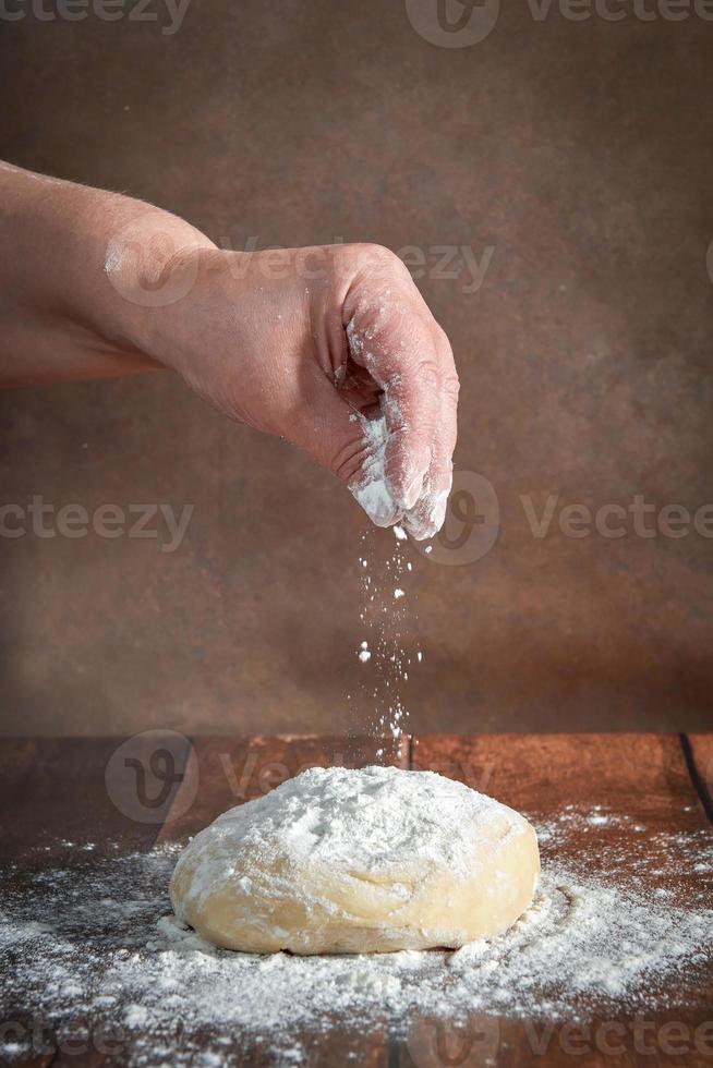 The hands of an elderly, plump woman are kneading dough on a wooden table. Preparation of dough for a festive cake, pizza photo