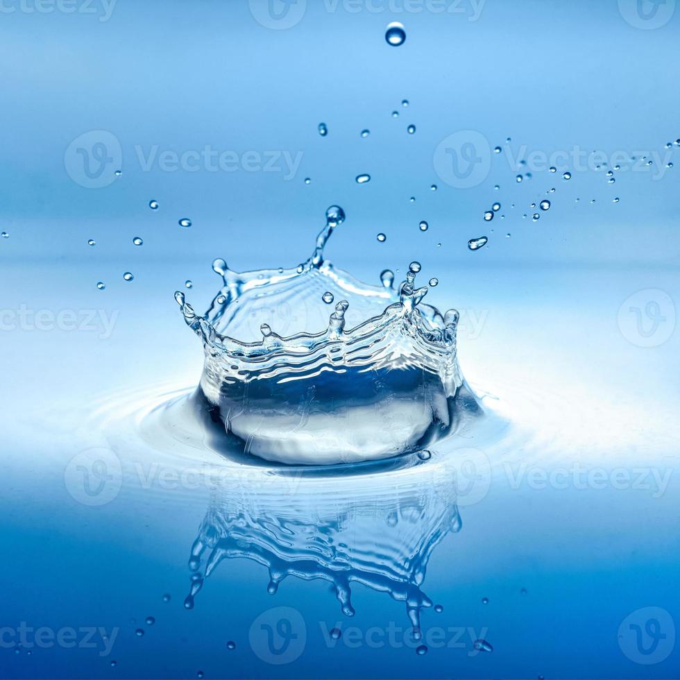 salpicaduras de agua con reflejo y gotas sobre un fondo azul foto