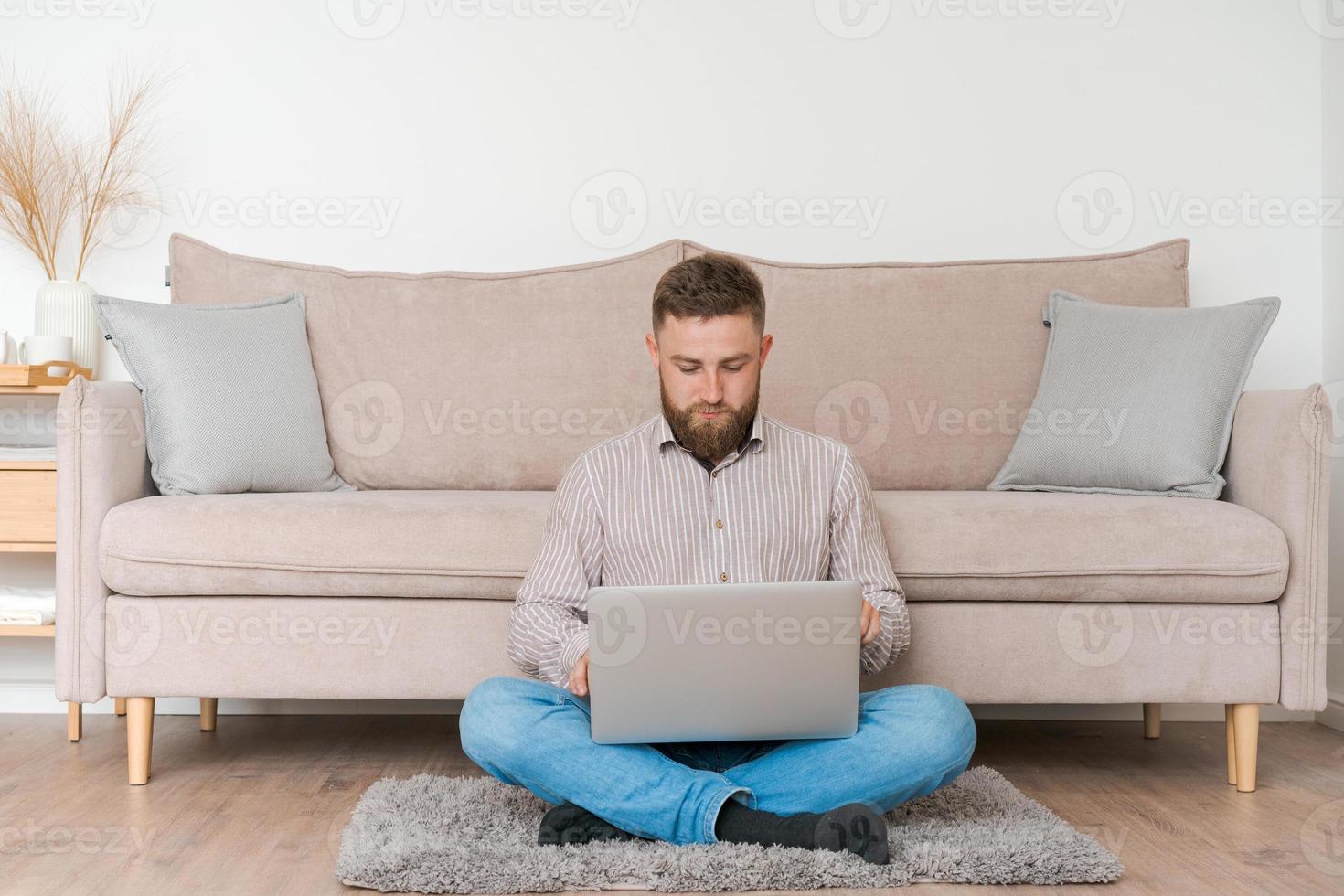 Young attractive man sitting on sofa at home, working on laptop online, using photo
