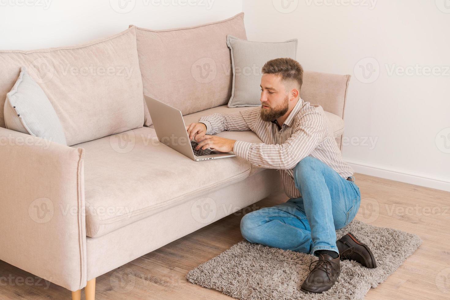 Young attractive man sitting on sofa at home, working on laptop online, using photo