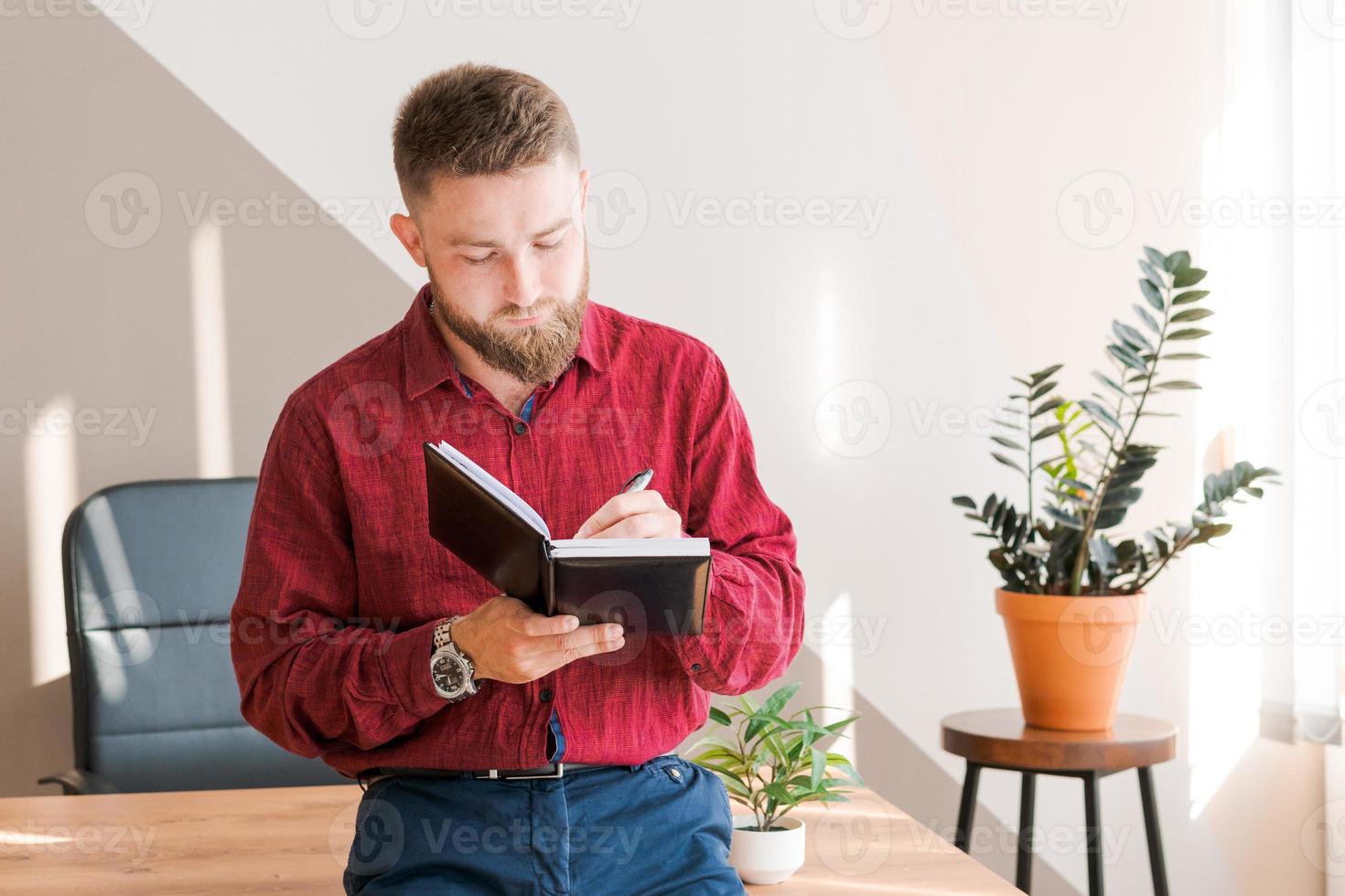 Budget planning. Pensive bearded man writing in a notebook while sitting photo