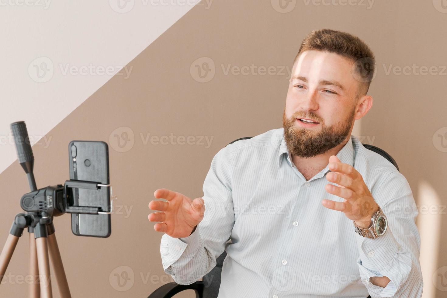 hombre de negocios barbudo sonriente, filmando su episodio de blog de video usando un teléfono inteligente foto