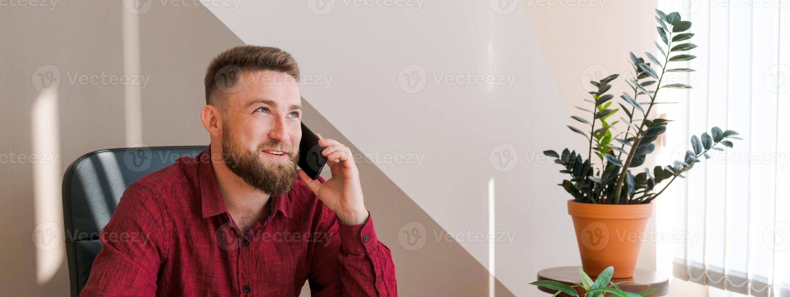Happy businessman at his desk in office talking on phone. A young businessman photo
